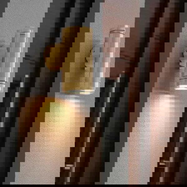 exterior brass wall lamp mounted on a white textured wall next to a wooden front door