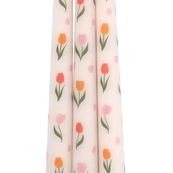 Close-up of tulip-print taper candles with orange and pink flowers on pale background