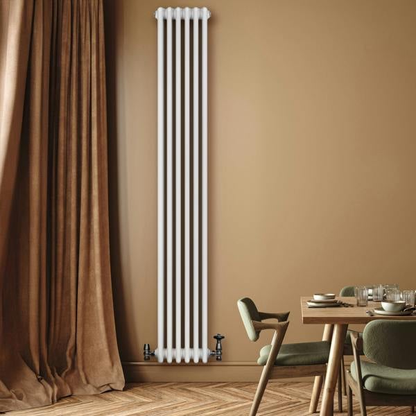 Tall white traditional 4 column radiator with sleek lines and black valves, mounted on a warm-toned wall beside a wooden dining table