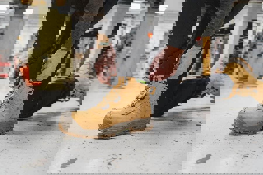 Apache Churchill Mens FIT GO Composite Toe S7S Safety Ankle Boots, Worker adjusting the laces of tan safety boots in a workshop setting.