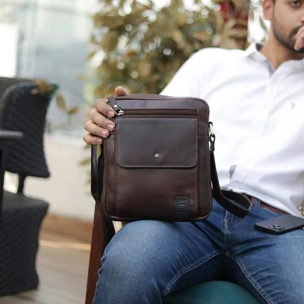 Man holding a brown leather crossbody bag outdoors