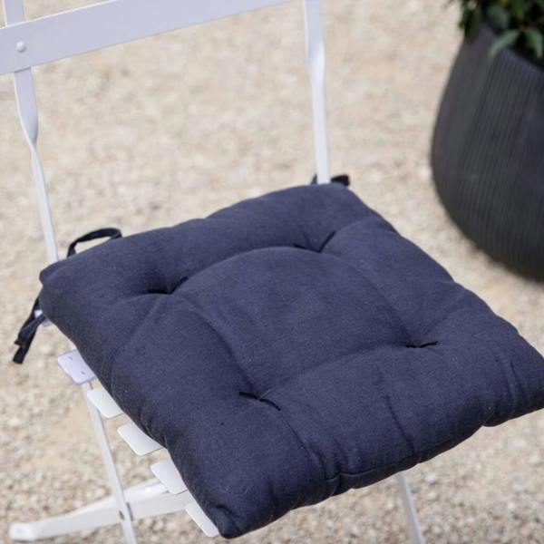 A deep carbon grey quilted linen seat pad cushion with corner ties attached to a white folding metal garden chair.