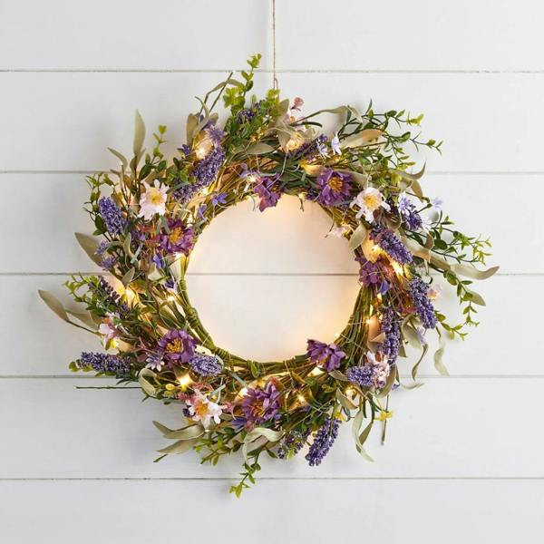 A 45cm spring wreath featuring faux purple lavender, wildflowers, and green foliage with glowing warm white micro LED lights, hanging on a white wooden shiplap wall.