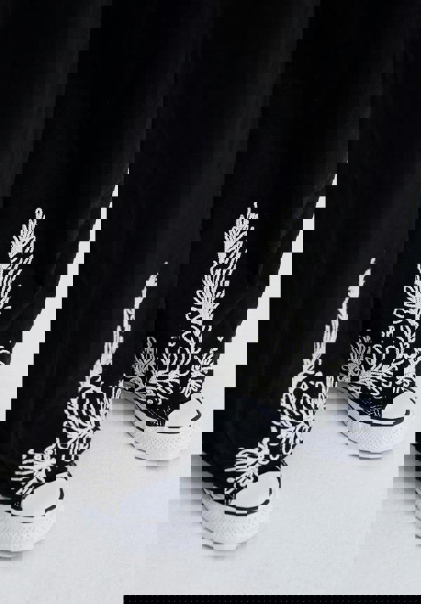 Black high-top sneakers with white floral patterns worn by a person.