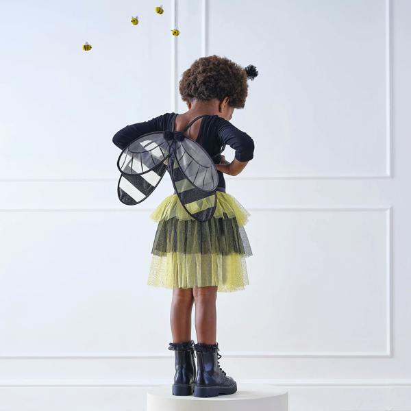 Full-length back view of a young child wearing a bumble bee costume with glittery wings, layered yellow and black tutu, and antenna headband.