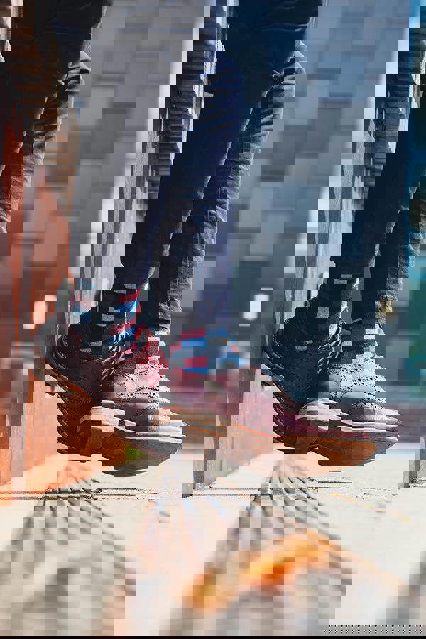 Person wearing brown shoes and patterned socks standing on a wooden floor with a blurred background.