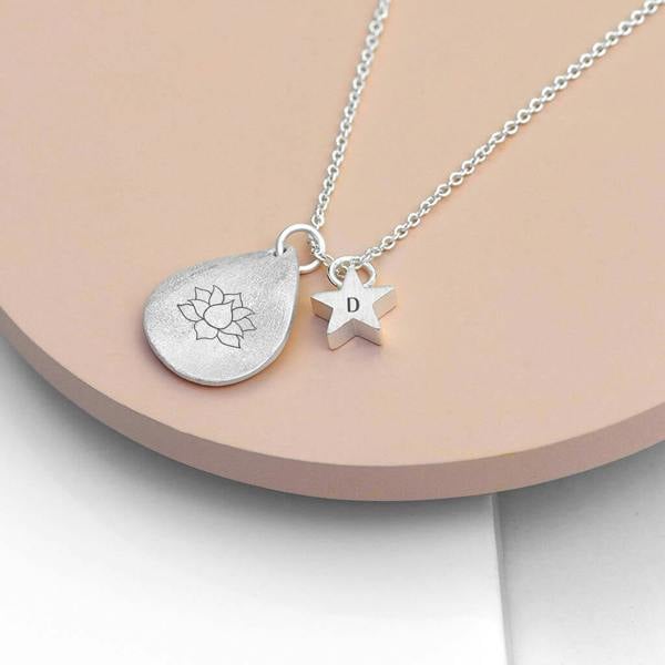 A silver-plated personalised lotus pendant necklace with an engraved initial star charm resting on a textured surface.