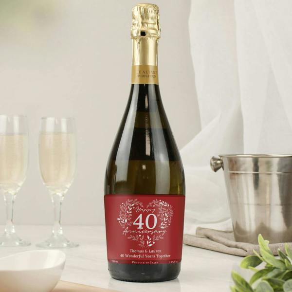 A bottle of Prosecco with a custom deep red label that reads 'Happy 40 Anniversary' in a white heart-shaped wreath, personalised with the names 'Thomas & Lauren'.