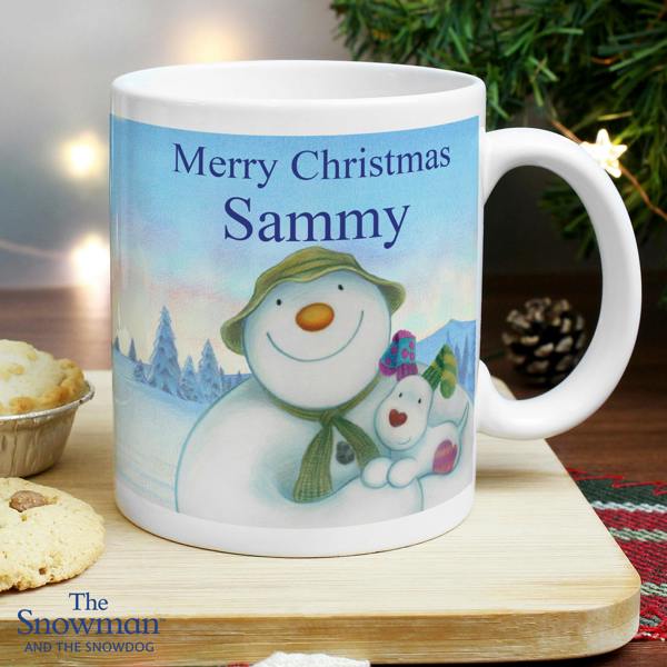 Personalised ceramic Christmas mug featuring The Snowman and the Snowdog artwork reading Merry Christmas Sammy on a wooden board next to cookies