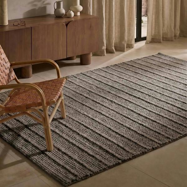 Woven rug on a tiled floor with a wooden sideboard and chair in the background.
