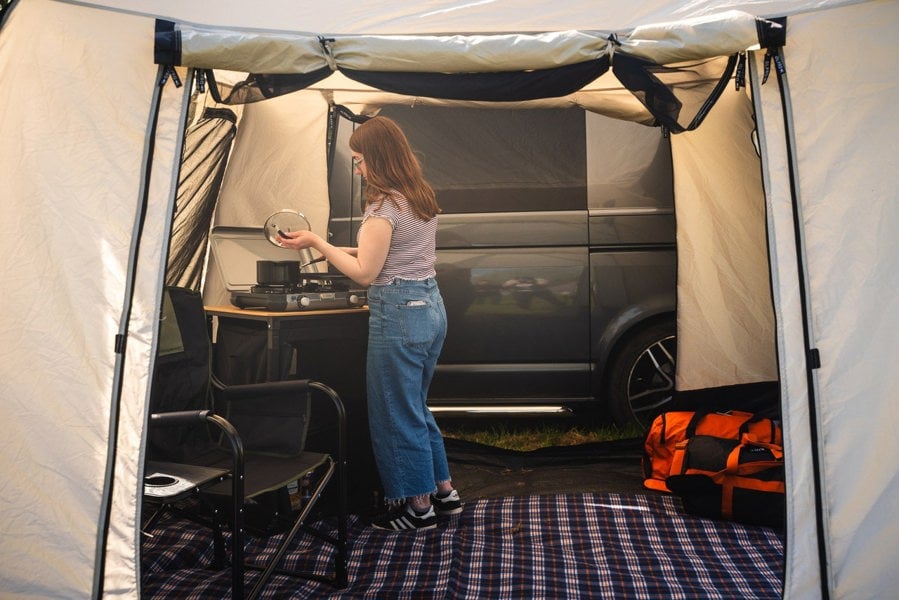 A young woman cooks on a CampinGaz stove atop a sustainable OLPRO Bamboo Camp Kitchen  Cubo Campervan Awning OLPRO