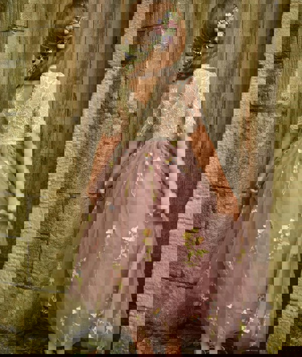 Young girl in a floral dress standing against a stone wall.