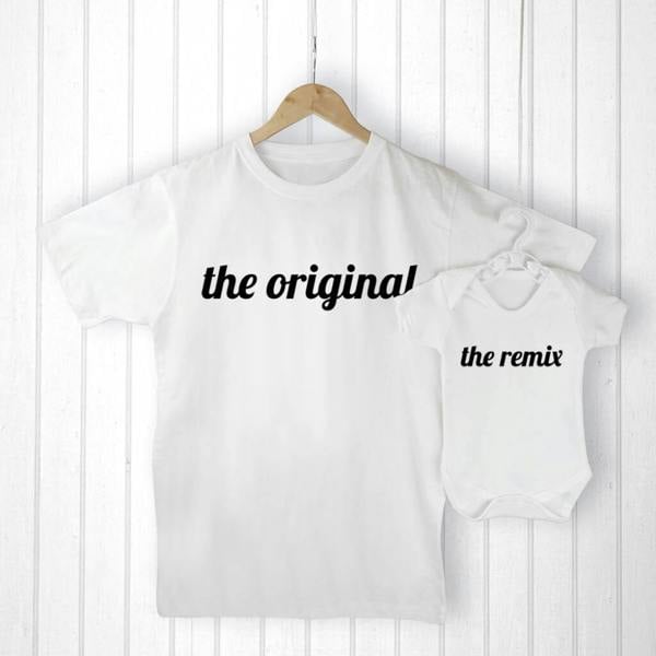 Flat lay photography of a crisp white men's "The Original" t-shirt hanging next to a matching smaller white baby "The Remix" bodysuit on wooden hangers, set against a bright white wooden paneled wall.