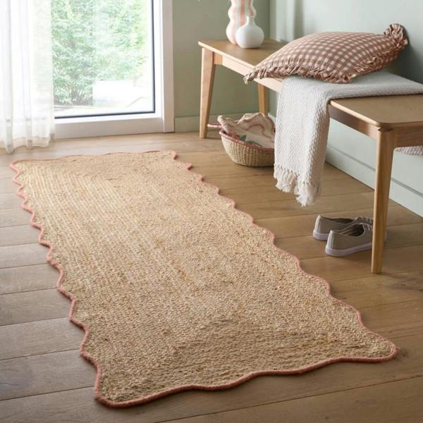 Beige woven rug on a wooden floor with a bench and window in the background
