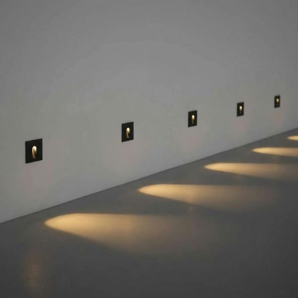 black outdoor step light fixture mounted in a row along a white wall outside