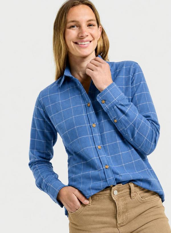 A woman wearing a blue long-sleeve button-up shirt with a white windowpane plaid pattern and tan pants, posing against a light gray studio background.