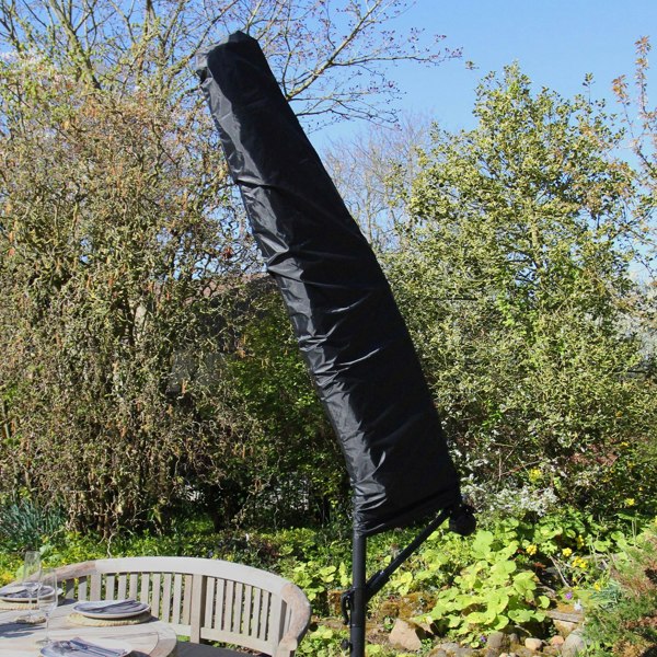 Black parasol cover standing upright beside a garden table, surrounded by greenery and sunlight, showcasing outdoor decor elements
