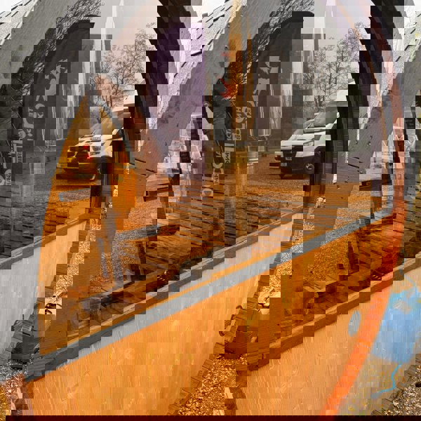 Outdoor barrel sauna with glass window and van reflection.