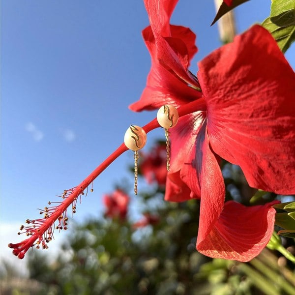 Gold drop earrings with freshwater pearls against a red hibiscus flower.