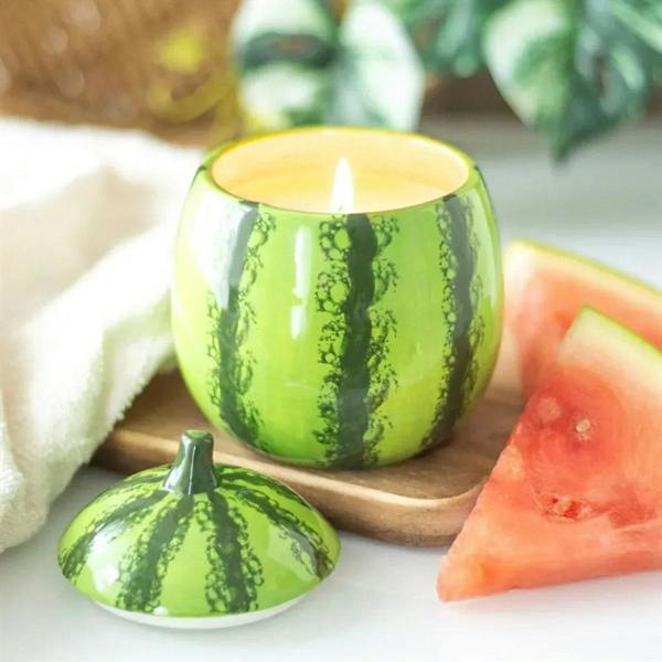Green watermelon-shaped candle jar, lid open with lit wick; matching green top.