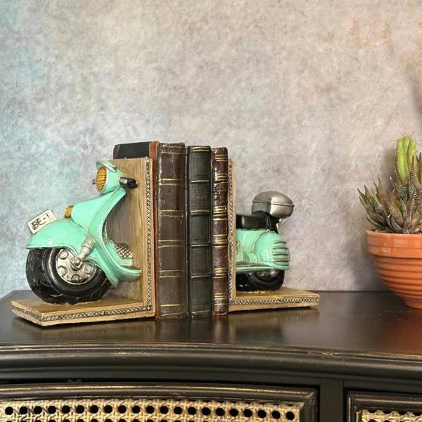 A pair of vintage mint green polyresin scooter bookends holding three antique books together on a dark wooden cabinet next to a potted succulent plant.