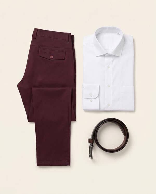 Maroon pants, white shirt, and brown belt arranged on a beige background