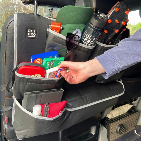 An adult male retrieving an item out of the OLPRO Rear Double Seat Storage Organiser in Grey that is full of summer themed items and attached to the back of the front seats of a camper van.