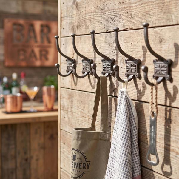 Close-up of five vintage cast iron Union Jack coat hooks mounted on rustic wooden wall with garden bar items hanging in bright natural light.