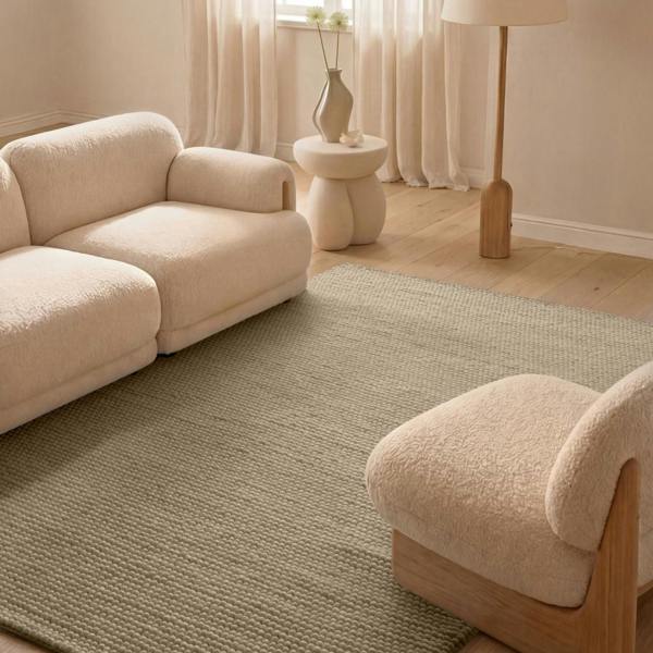 Beige sofa and chair in a living room with a textured rug and lamp.