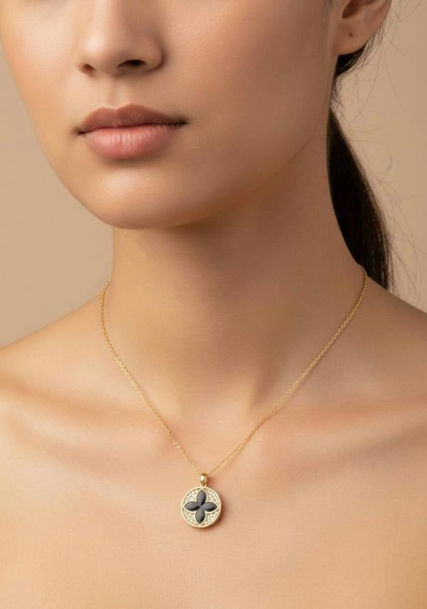 Close-up of a person wearing a gold necklace with a clover pendant on a beige background