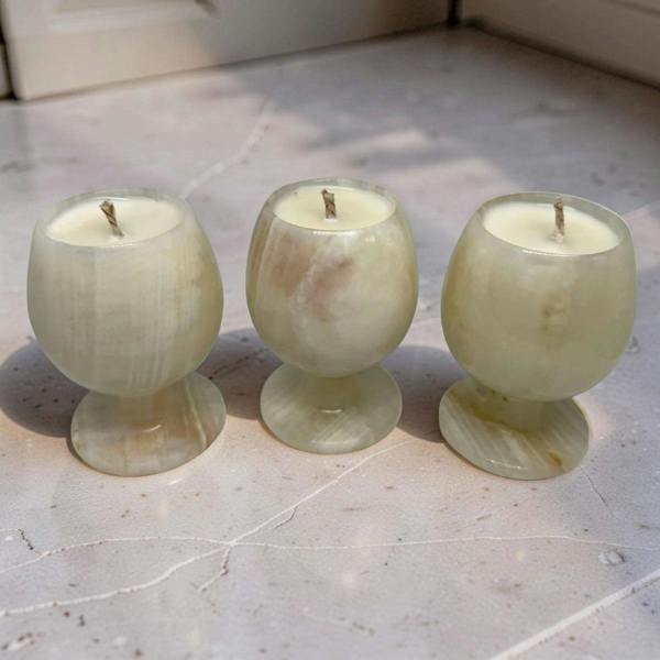 Three green onyx candle holders with candles on a light stone floor.