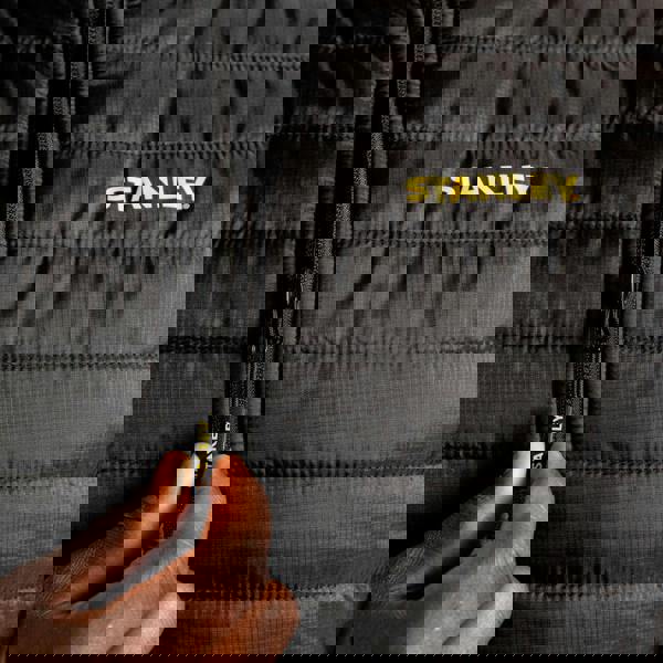 Stanley Banff Mens Ripstop Water Resistant Work Gilet Body Warmer, close-up view showing the black quilted fabric with yellow Stanley logo on the chest and a zipper pull with the Stanley branding.