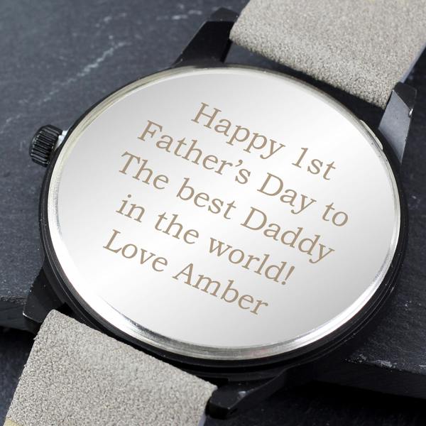 A close-up view of the stainless steel back of the personalized men's watch by Abode Home & Gifts, featuring a custom engraved message that reads 'Happy 1st Father's Day to The best Daddy in the world! Love Amber', resting on a dark slate background.
