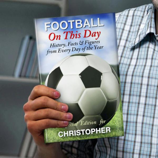 A close-up of a person holding the Personalised Football 'On This Day' Book, showing a large football graphic on a pitch under a blue sky, with a custom name printed at the bottom.