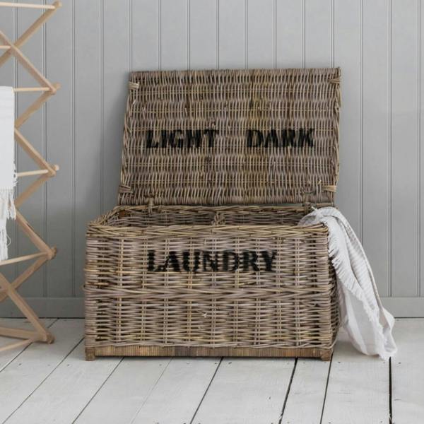 Open woven rattan laundry chest showing internal lights and darks labels on a white wooden floor.