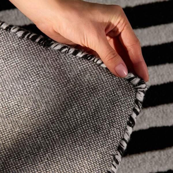 Hand holding a gray fabric with black trim against a striped background