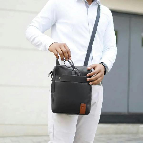 Person holding a black messenger 
 leather bag with a blurred background