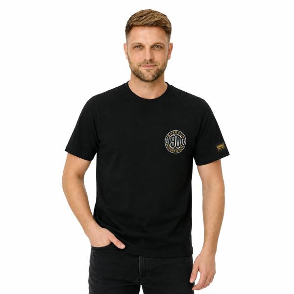 Man wearing a black Barbour International 90th Anniversary graphic t-shirt with a circular chest logo and sleeve tab.