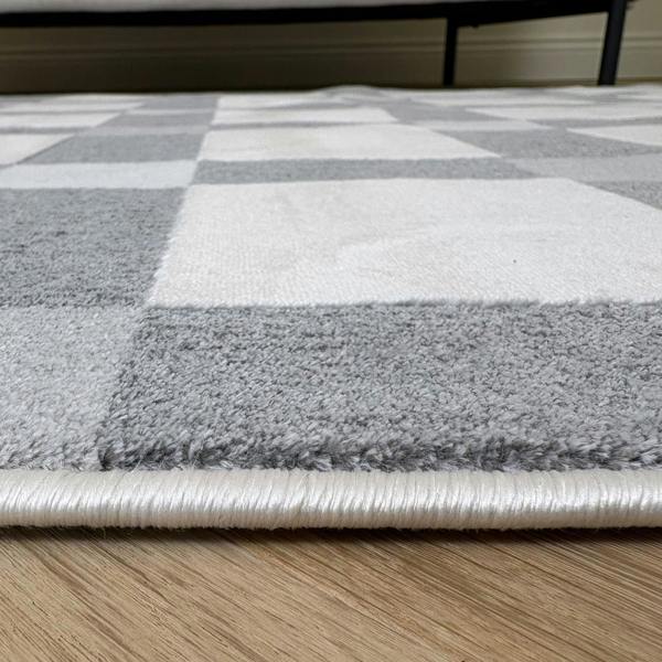 Close-up of a checkered area rug with gray, white, and beige squares on a wooden floor.