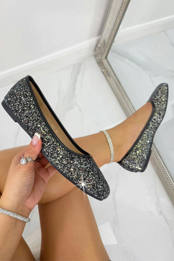 Black glittery flats worn by a person sitting on a white surface.