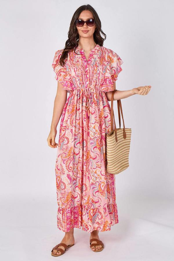 Woman wearing a pink patterned dress holding a straw bag on a white background