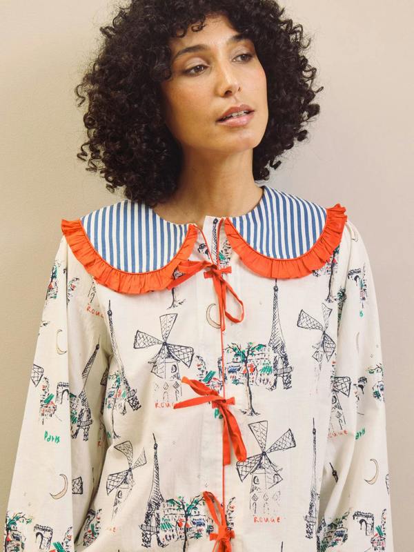 Woman wearing a Paris themed printed pyjama set with a large collar with red frill against a beige background