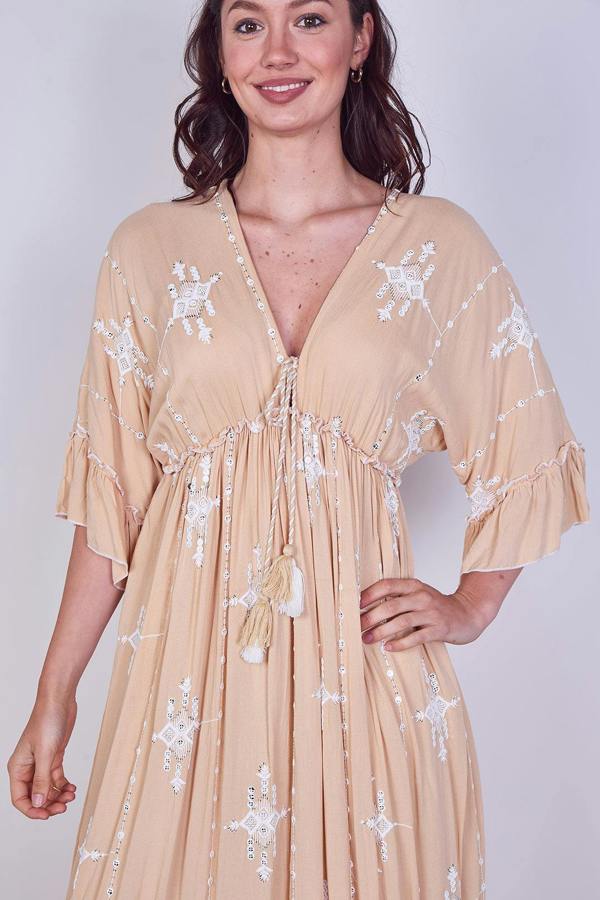Woman wearing a beige dress with white floral embroidery on a plain background