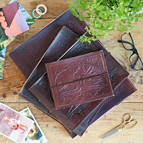 A stack of handmade, naturally dyed Leather Tree of Life Embossed Photo Albums on a wooden table.