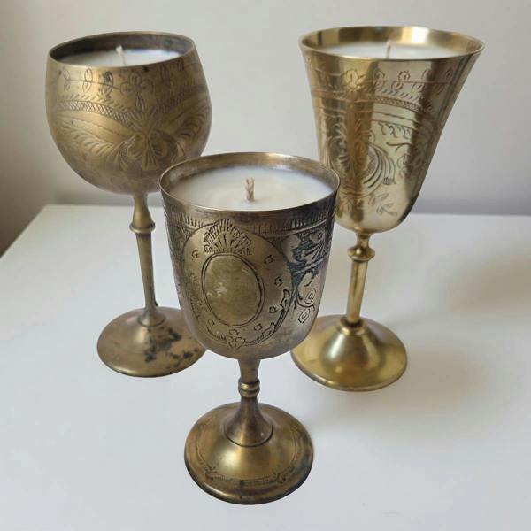 Three ornate brass candle holders with candles inside on a white surface.
