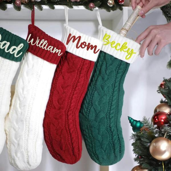 Four personalised embroidered cable-knit Christmas stockings in green, red, and white hanging on a mantelpiece