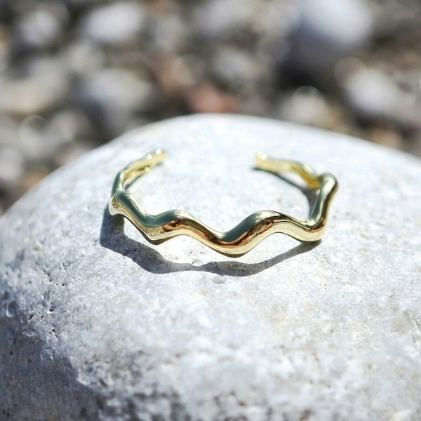 Gold vermeil wavy cuff by LENAE London on a rock.