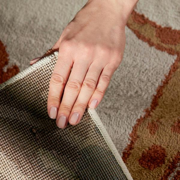 Hand pulling a rug off the floor with a patterned rug underneath