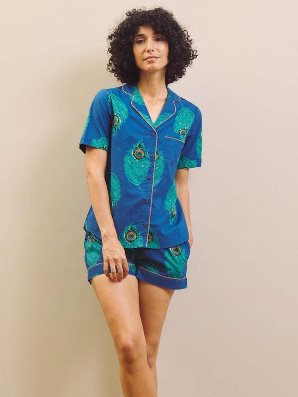 Woman wearing a blue peacock patterned shirt pyjama set against a beige wall.