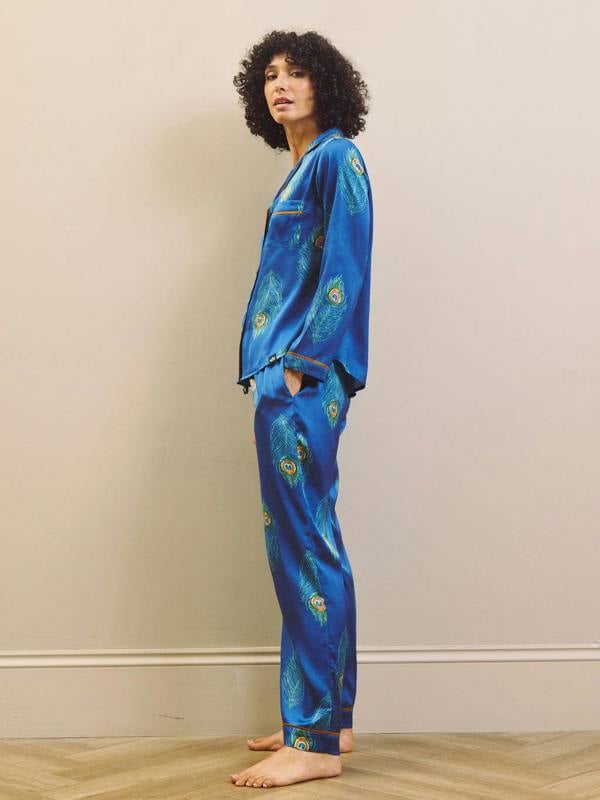 Person wearing a blue satin pajama set with peacock patterns on a beige background
